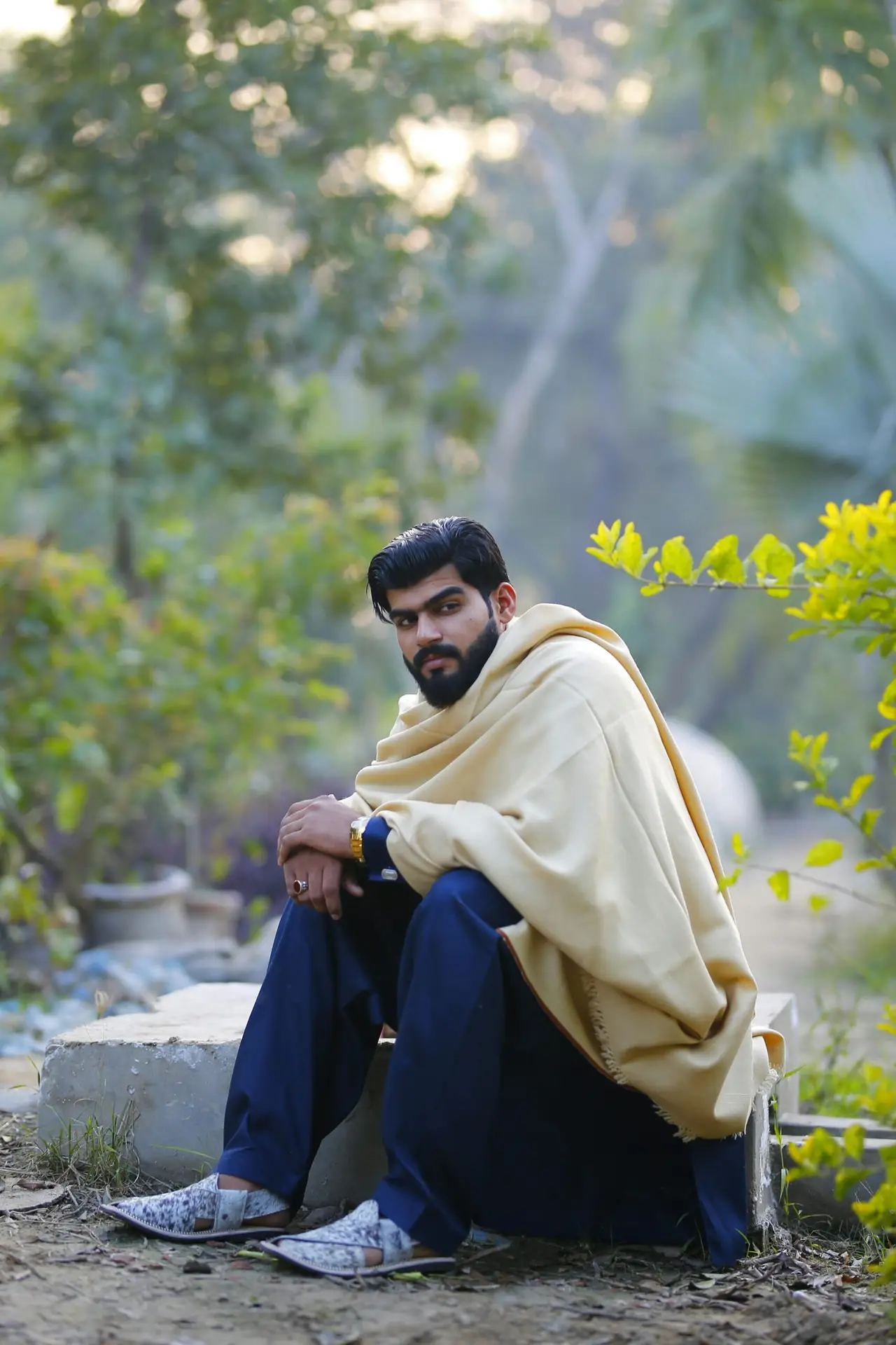 Man in traditional attire sits outdoors in a park with greenery, conveying a serene, cultural ambiance.